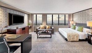 Habitación de hotel con una cama grande, un sofá, un televisor, un escritorio y vistas a la ciudad.