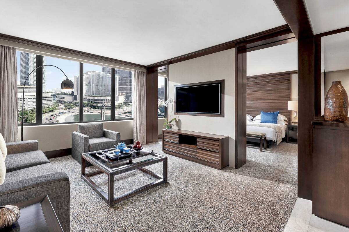 Una habitación de hotel moderna con vista a la ciudad, televisor de pantalla plana, sofá, mesa de centro y cama con mesita de noche.