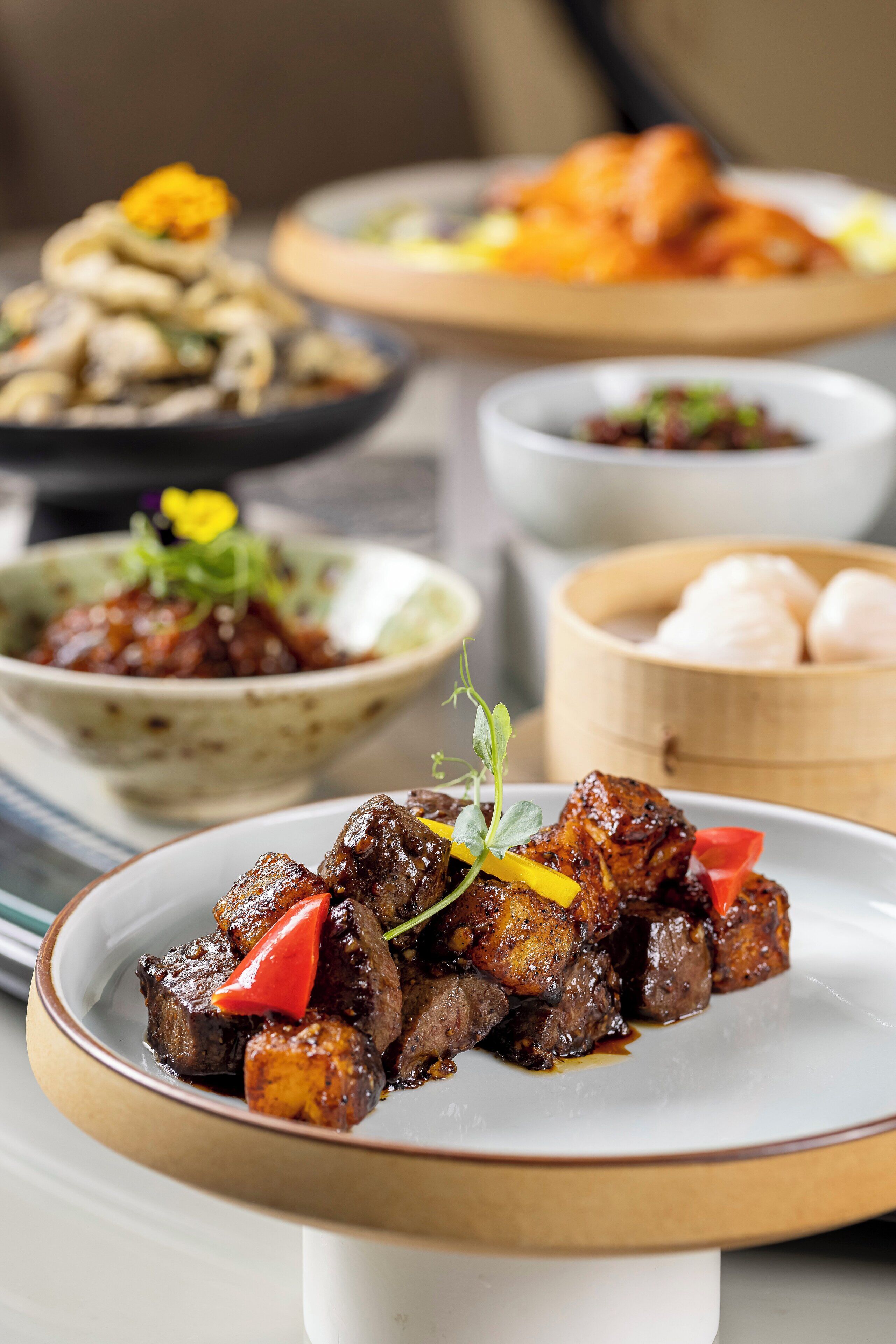 A variety of dishes on a table, including a plate with meat and vegetables, a bowl of soup, and a plate with dumplings.