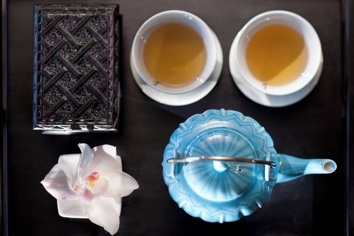 Una bandeja con dos tazas de té, una tetera azul, una caja decorativa y una orquídea blanca.