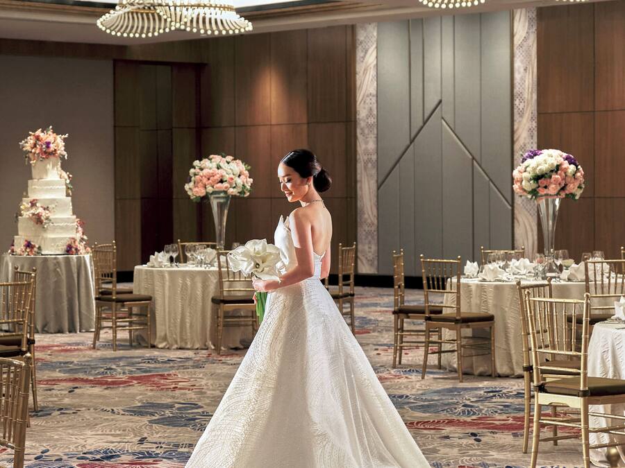 Un salón de bodas con una novia en un vestido blanco, mesas preparadas para una recepción y una elaborada tarta de bodas.