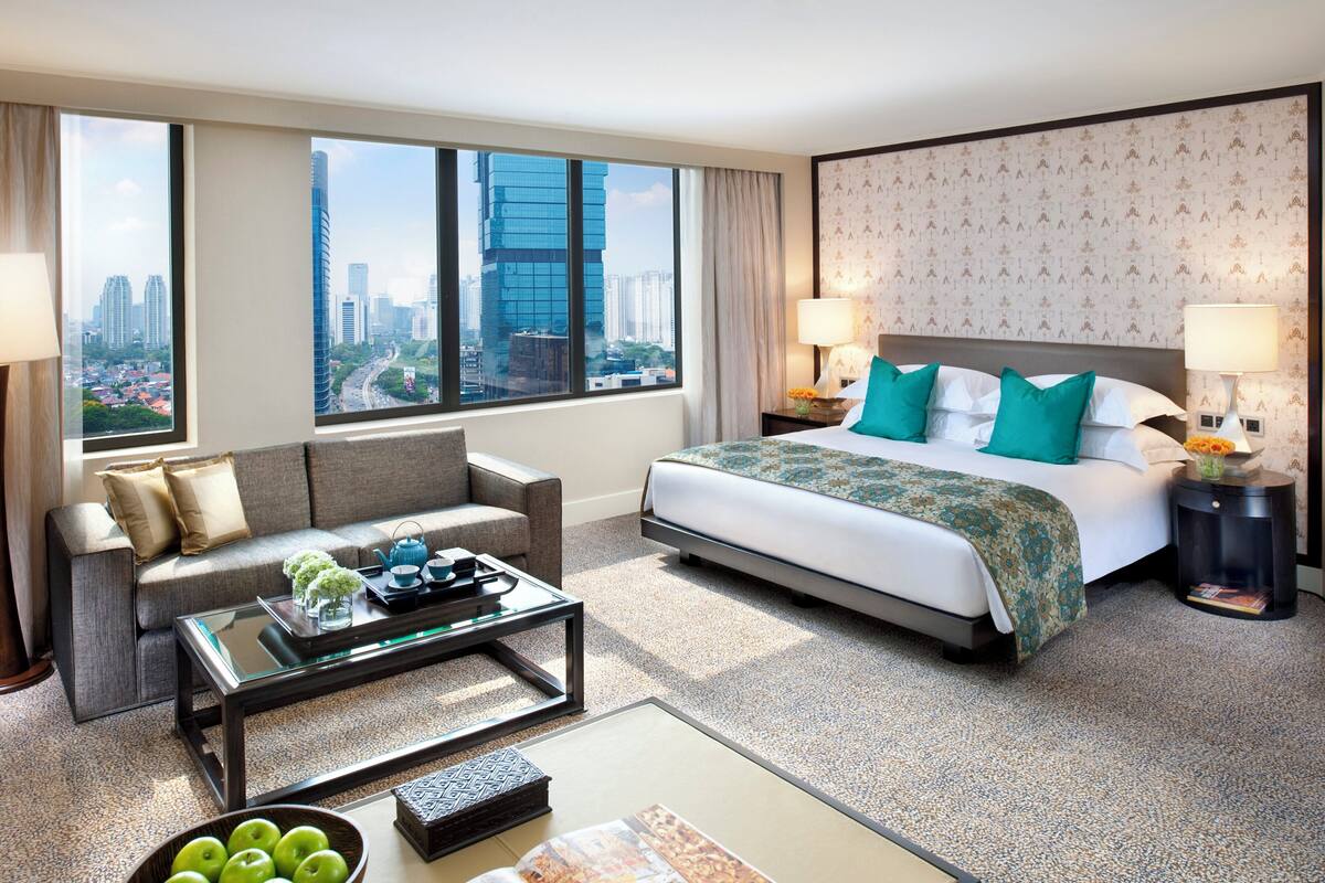 Habitación de hotel con una cama grande, un sofá, una mesita de centro y vistas a la ciudad.