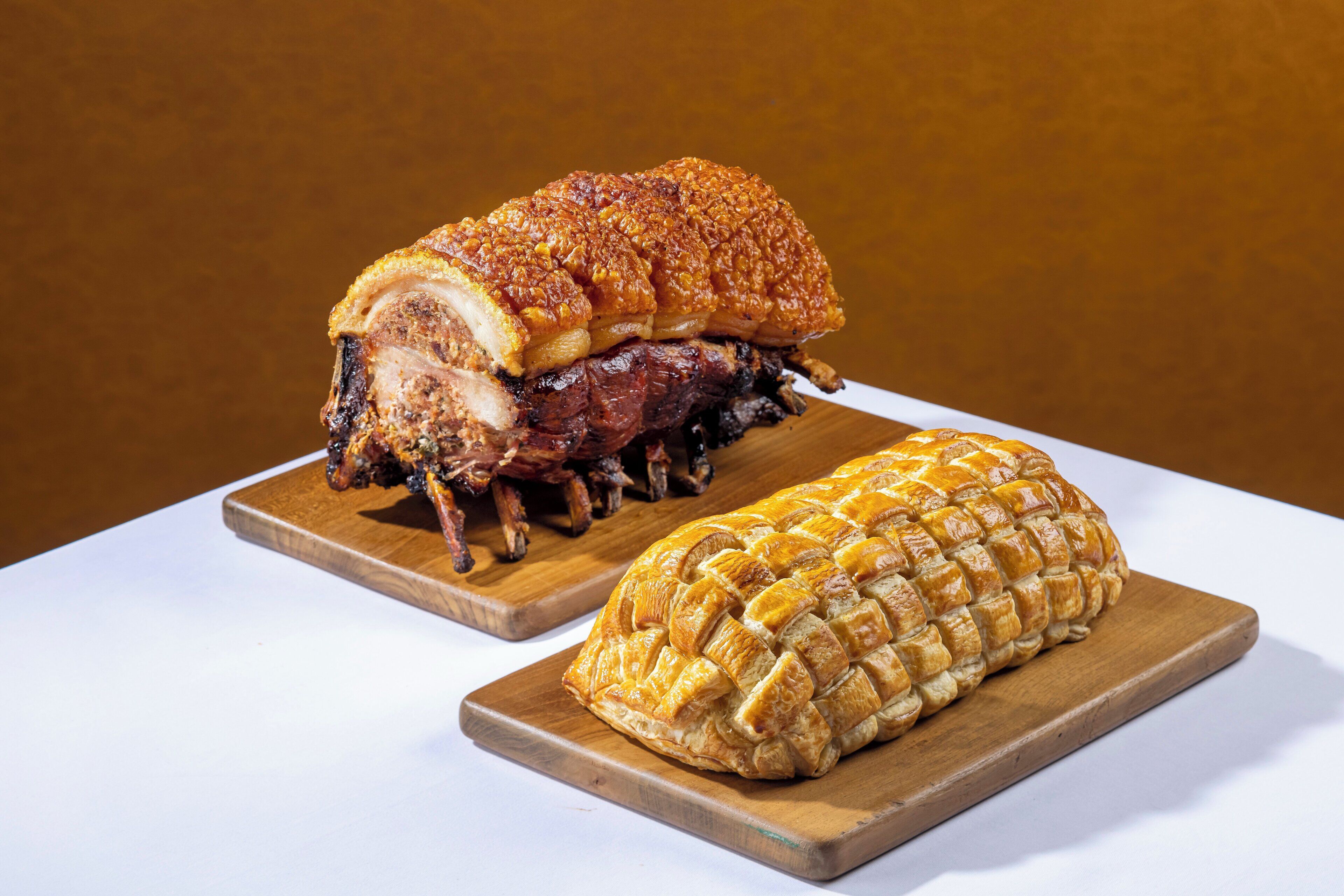 A roasted pork leg and a breaded meat on wooden boards.