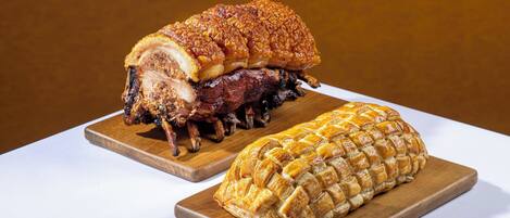A roasted pork leg and a breaded meat on wooden boards.