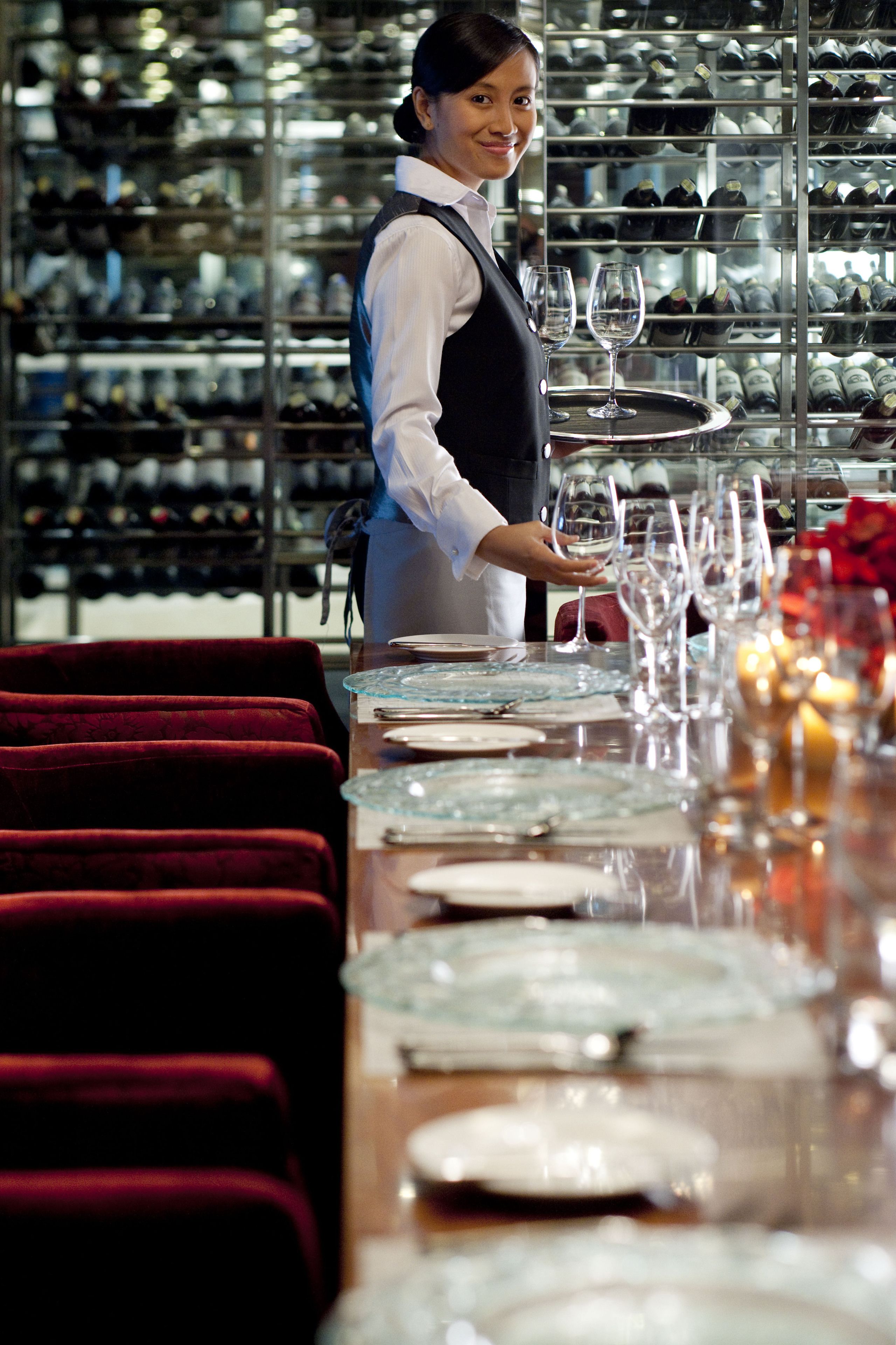 Un restaurante con un camarero disponiendo copas de vino en una bandeja.