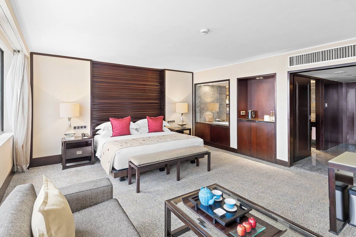 Una habitación de hotel con cama, mesitas de noche, un banco, una mesa de centro con bandeja y un espejo.