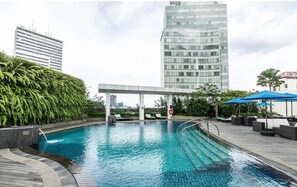 A rooftop pool with a view of tall buildings, a covered seating area, and a lush green hedge. - Mandarin Oriental, Jakarta (Jakarta)