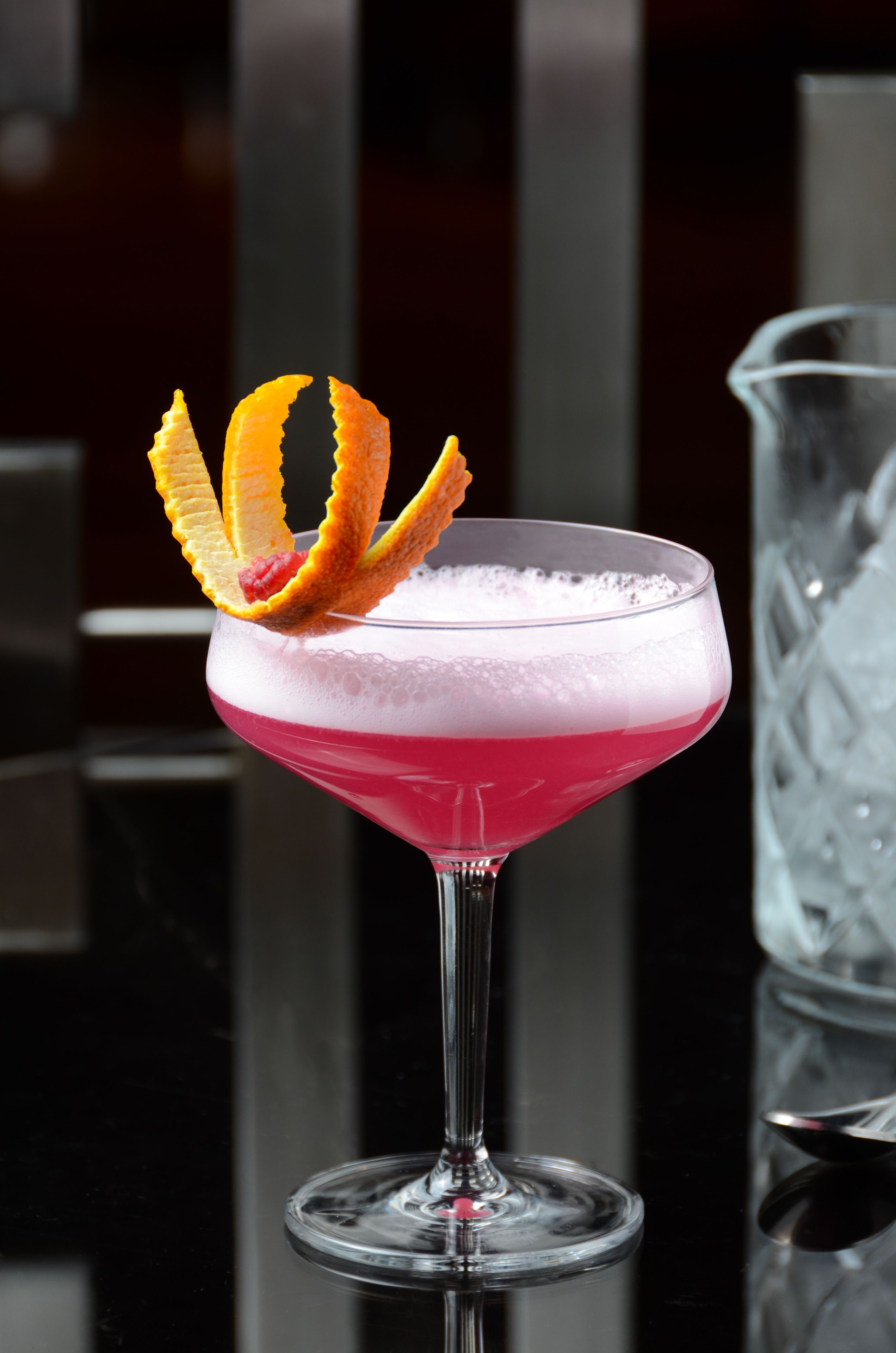 Un cocktail à la mousse onctueuse, garni d’un zeste d’orange, servi dans un verre à martini.