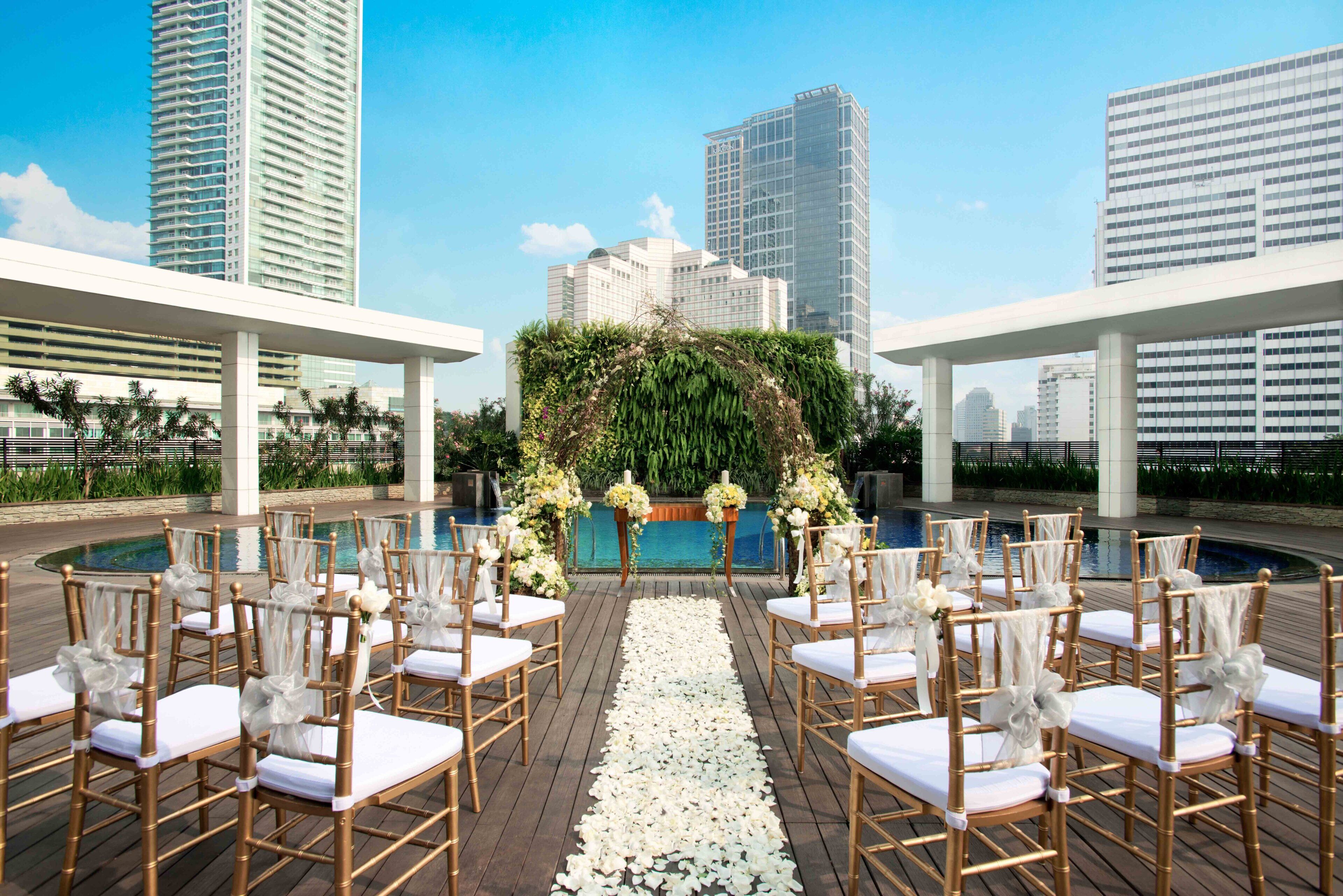 Decoração de casamento ao ar livre com piscina, flores e vista para prédios da cidade.