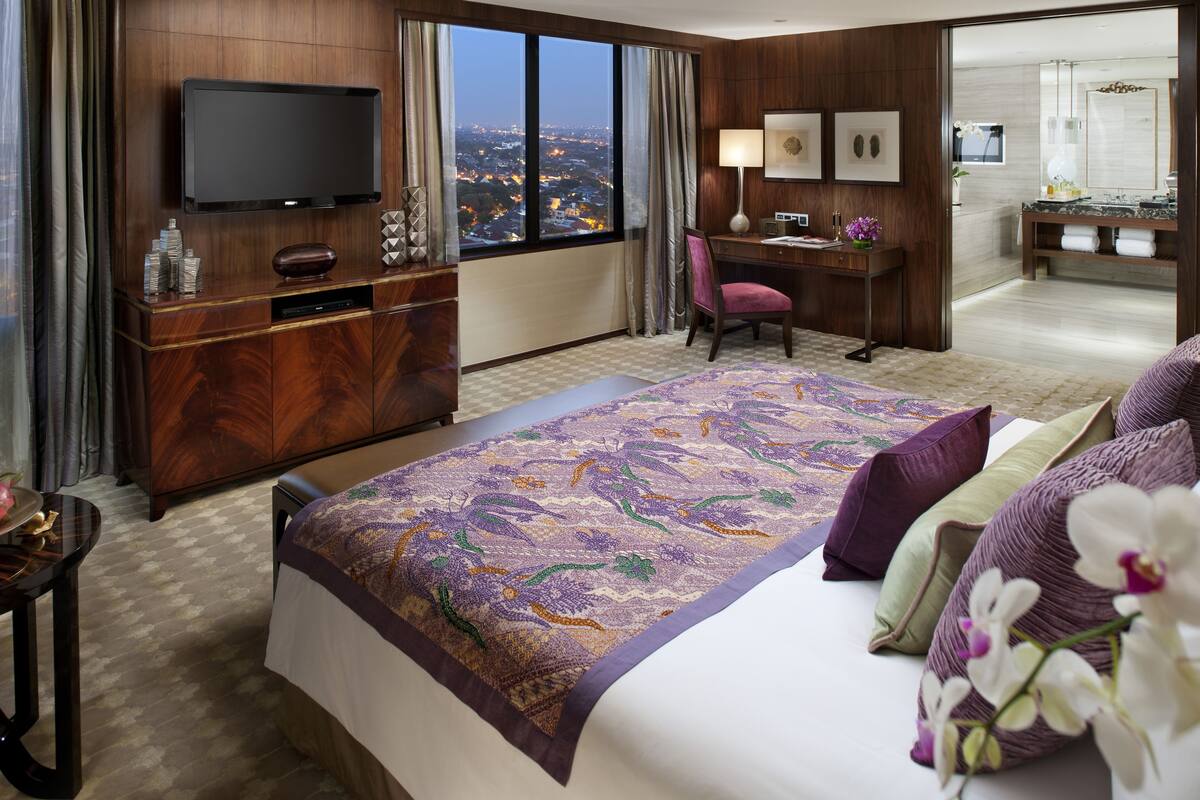 Habitación de hotel con una cama grande, un escritorio, televisión y vistas a la ciudad.