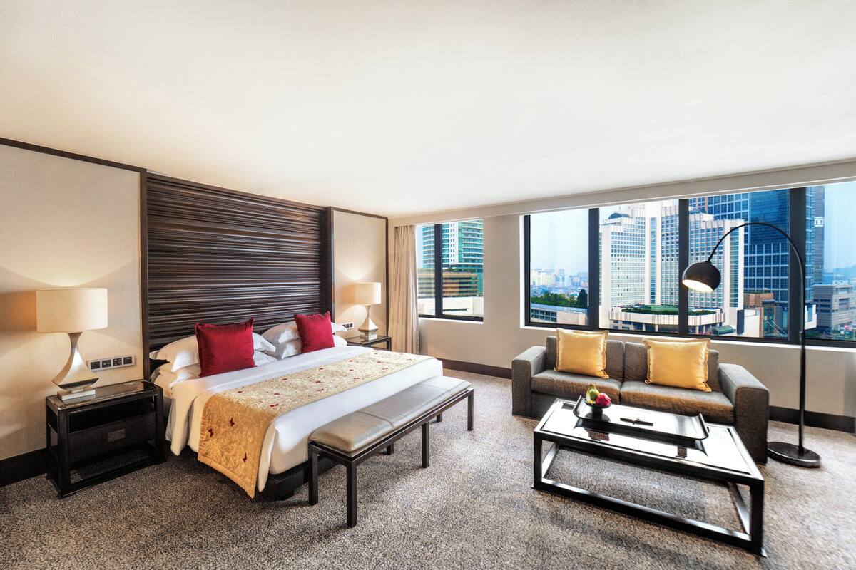 Habitación de hotel con una cama grande, un sofá, una mesa de centro y vistas a la ciudad.