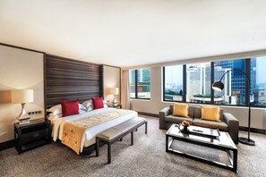 Habitación de hotel con una cama grande, un sofá, una mesa de centro y vistas a la ciudad.
