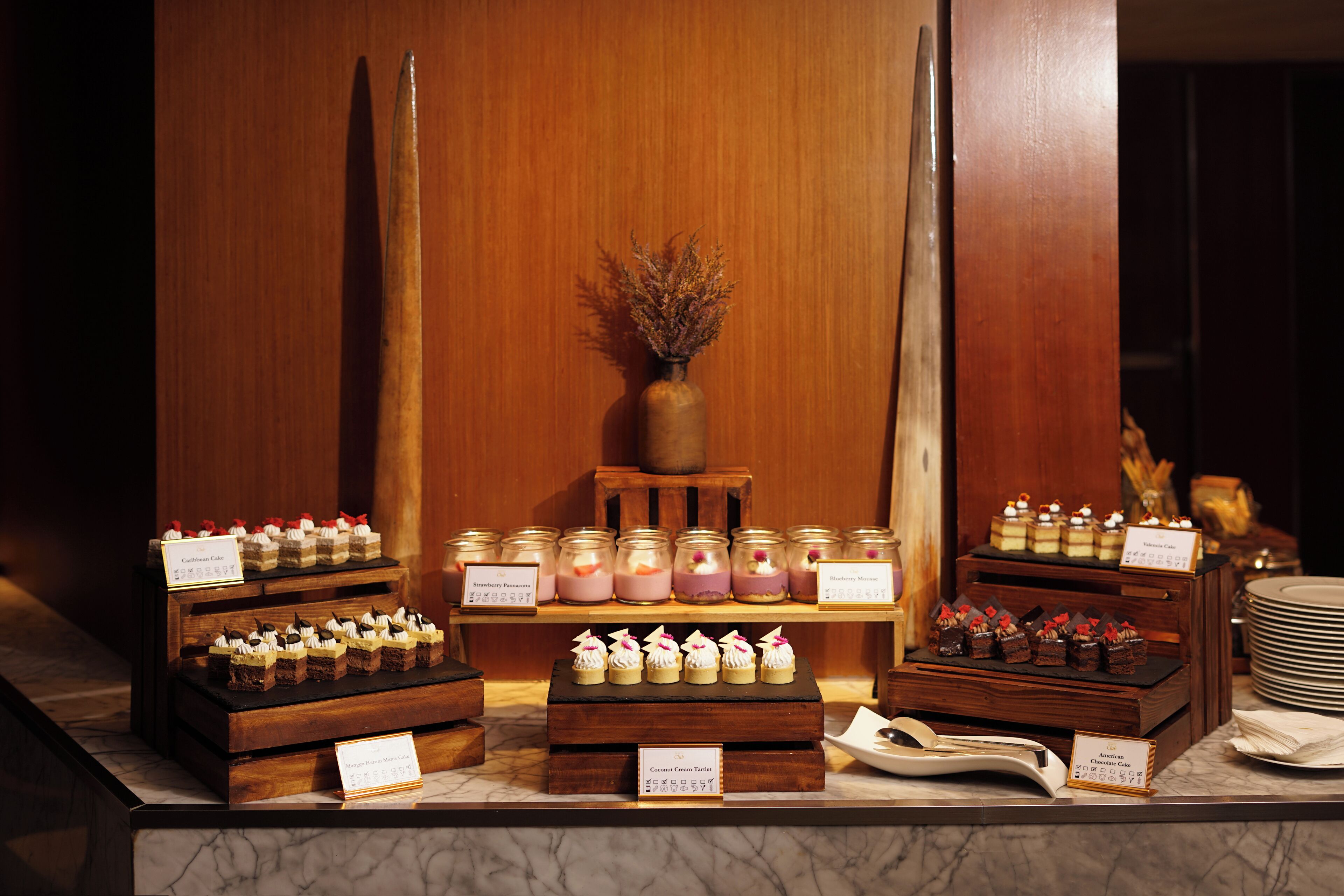 A dessert display with various cakes and pastries, each labeled with their names.