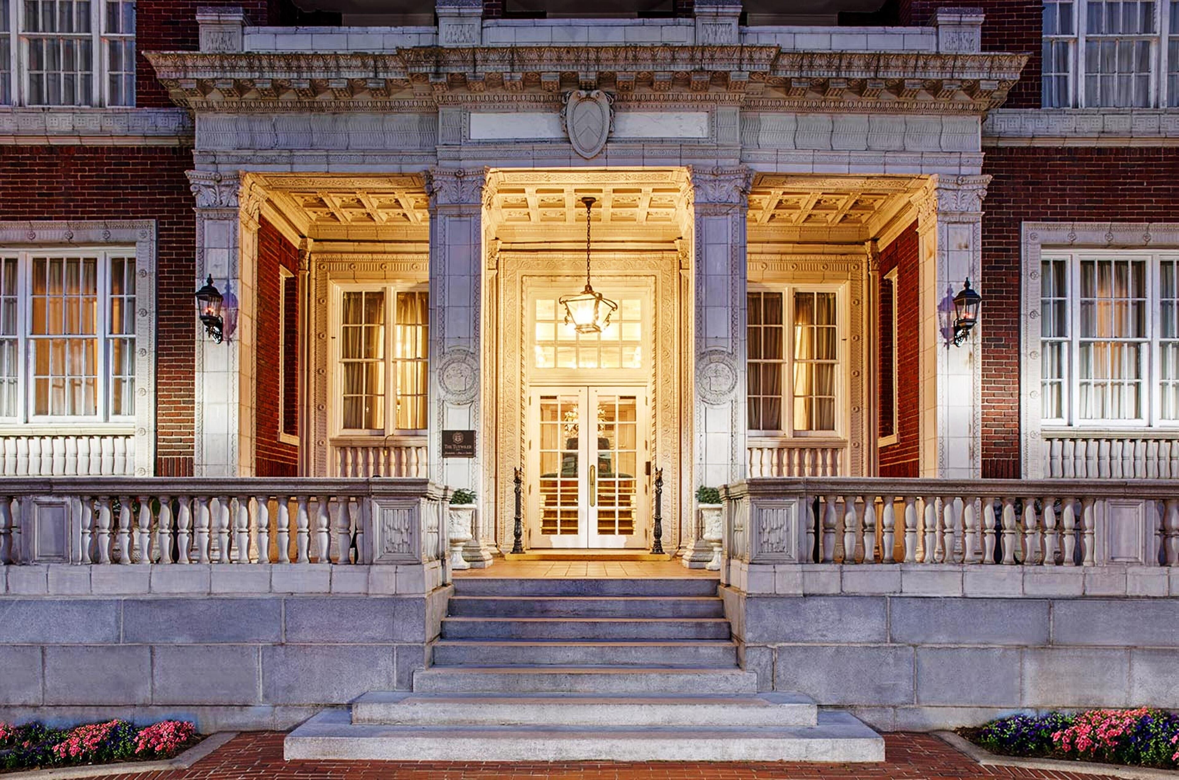 Imponente entrada con una escalera central que conduce a una puerta doble, flanqueada por columnas y una barandilla.