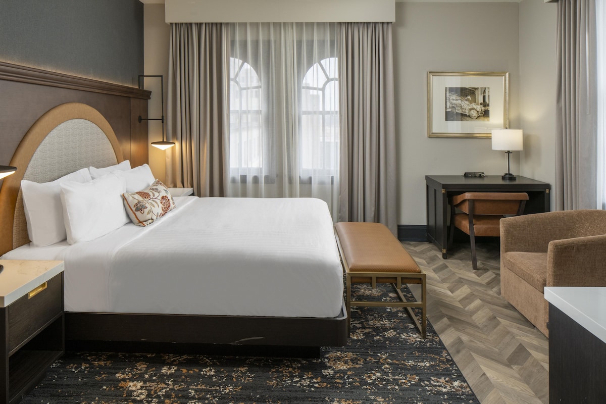 Une chambre d’hôtel avec un grand lit, un bureau, une chaise et un banc.