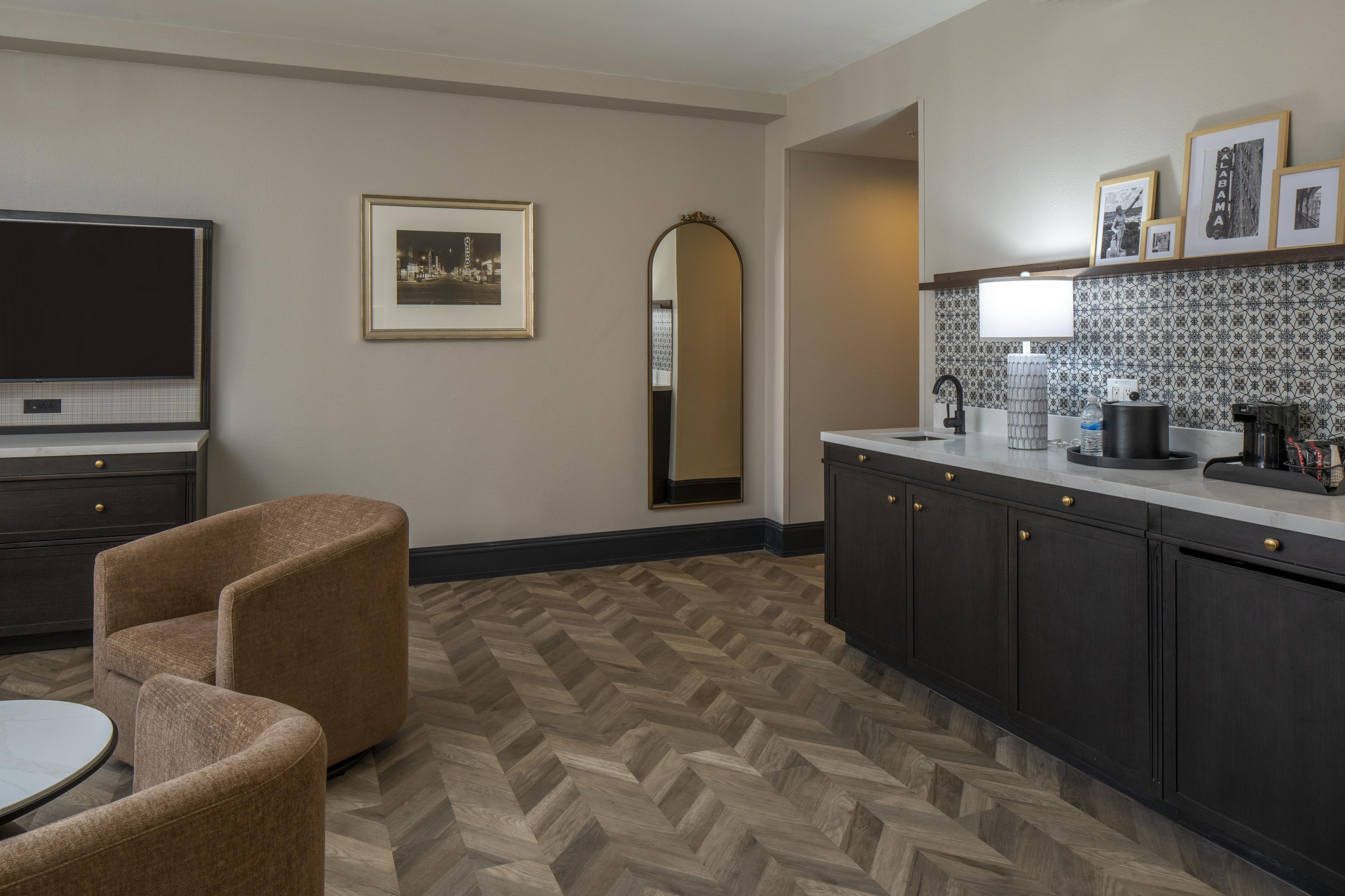 Une cuisine moderne avec un parquet à motifs en chevrons, des meubles de rangement sombres, un téléviseur à écran plat et un coin repas comprenant une table ronde et deux chaises.