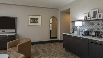 Une cuisine moderne avec un parquet à motifs en chevrons, des meubles de rangement sombres, un téléviseur à écran plat et un coin repas comprenant une table ronde et deux chaises.