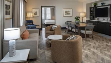 A hotel room with a sofa, armchair, dining table, and kitchen area.