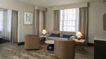 Quarto de hotel com sofá, duas poltronas, mesa de centro, abajur e um quadro na parede.