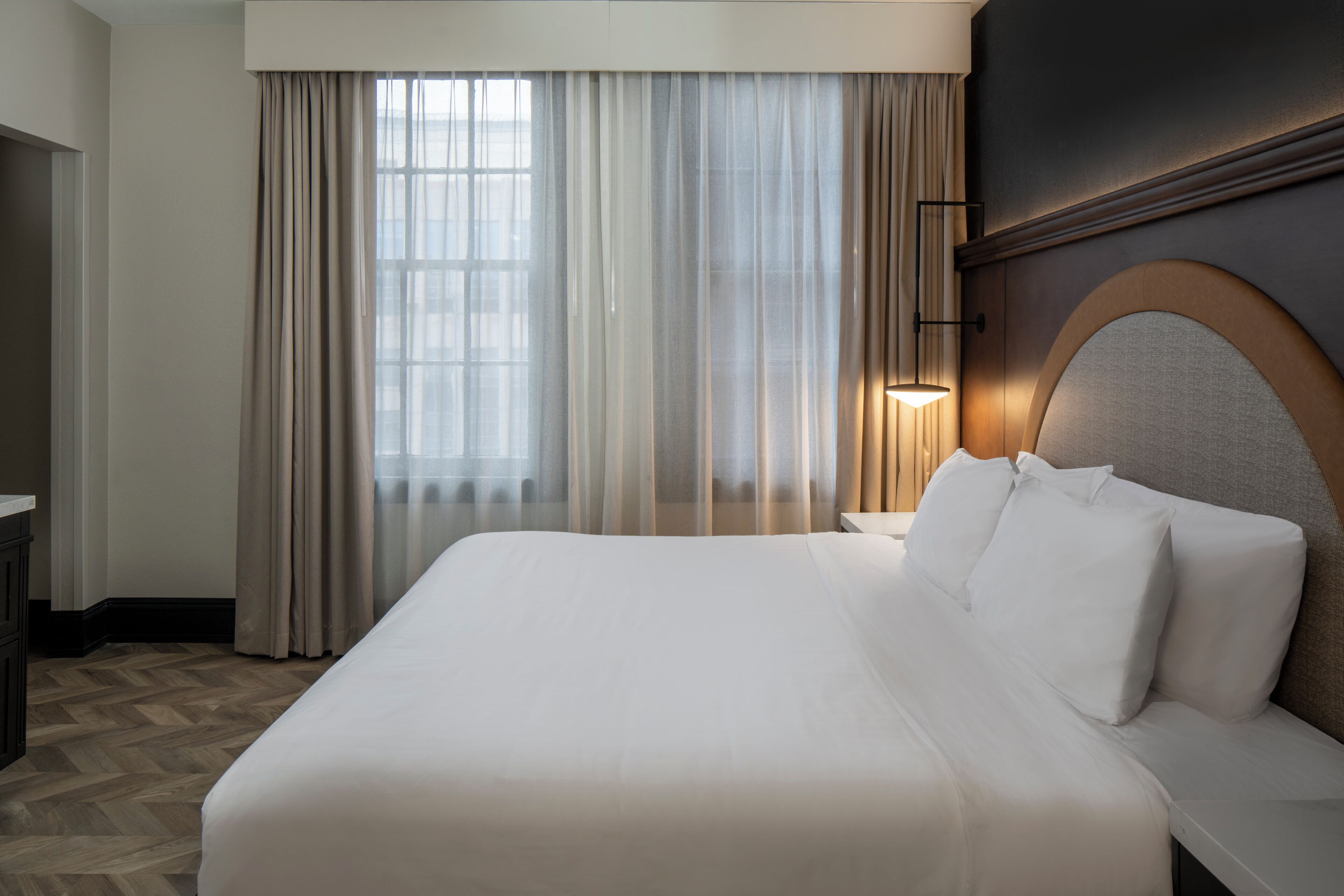 A hotel room with a large bed, a nightstand, a lamp, and a window with curtains.