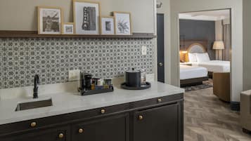 A hotel room with a kitchenette, a bed, a sitting area, and a bathroom.