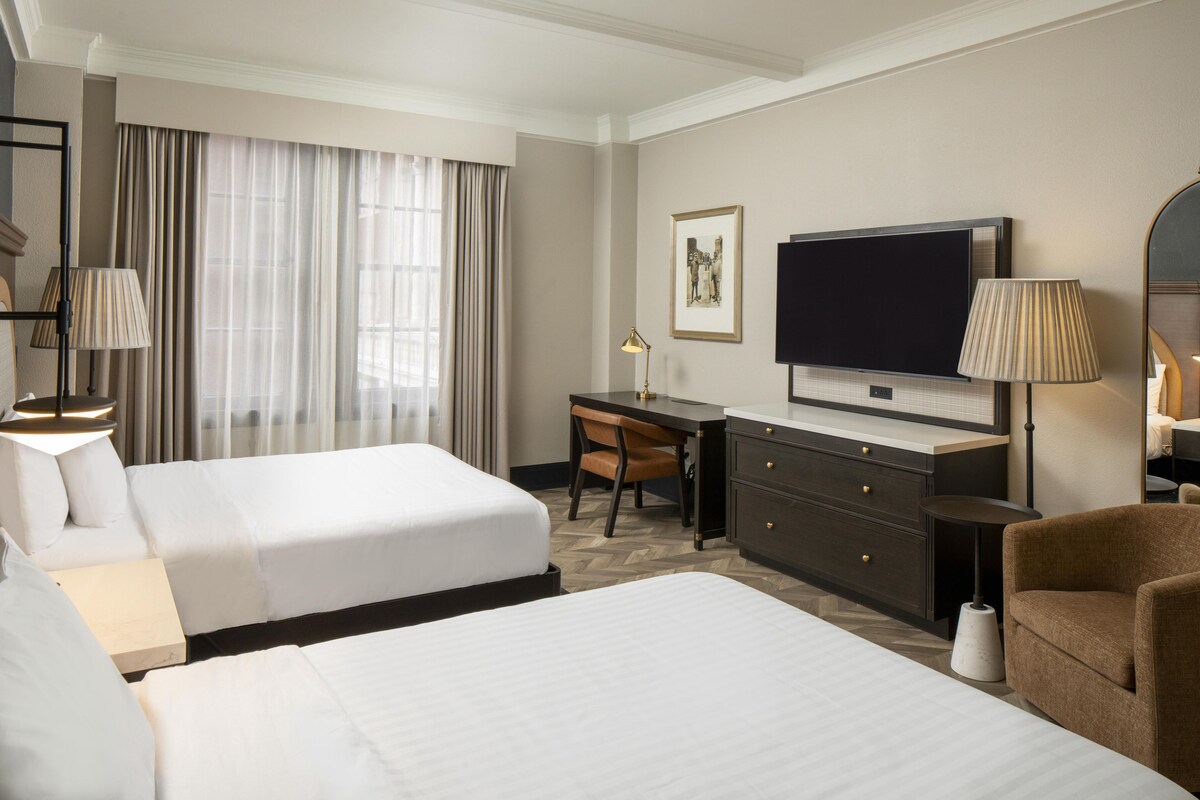 Une chambre d’hôtel avec deux lits, un bureau, une télévision et une chaise.