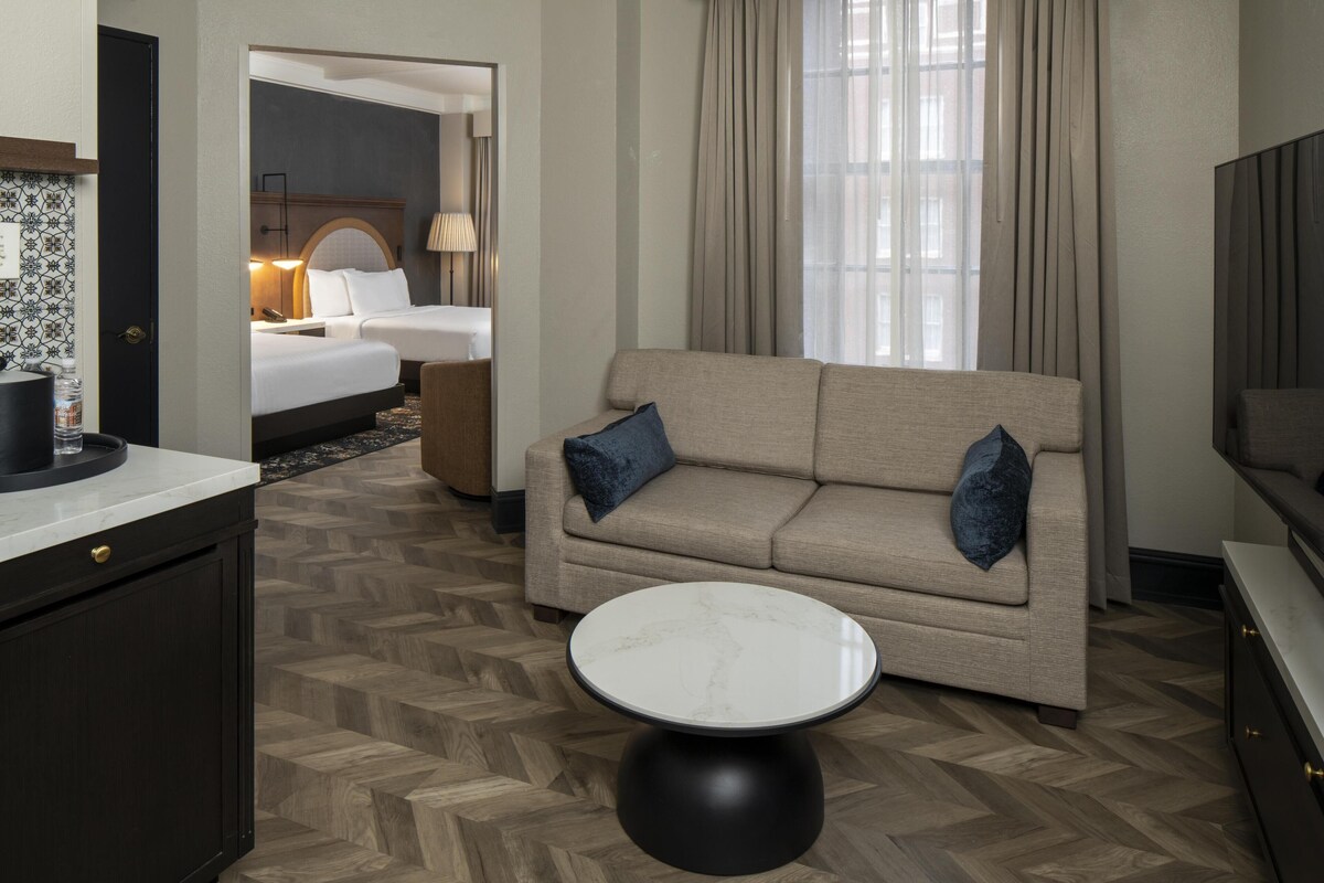 A hotel room with a sofa, a round coffee table, a bed, and a bathroom visible through an open door.