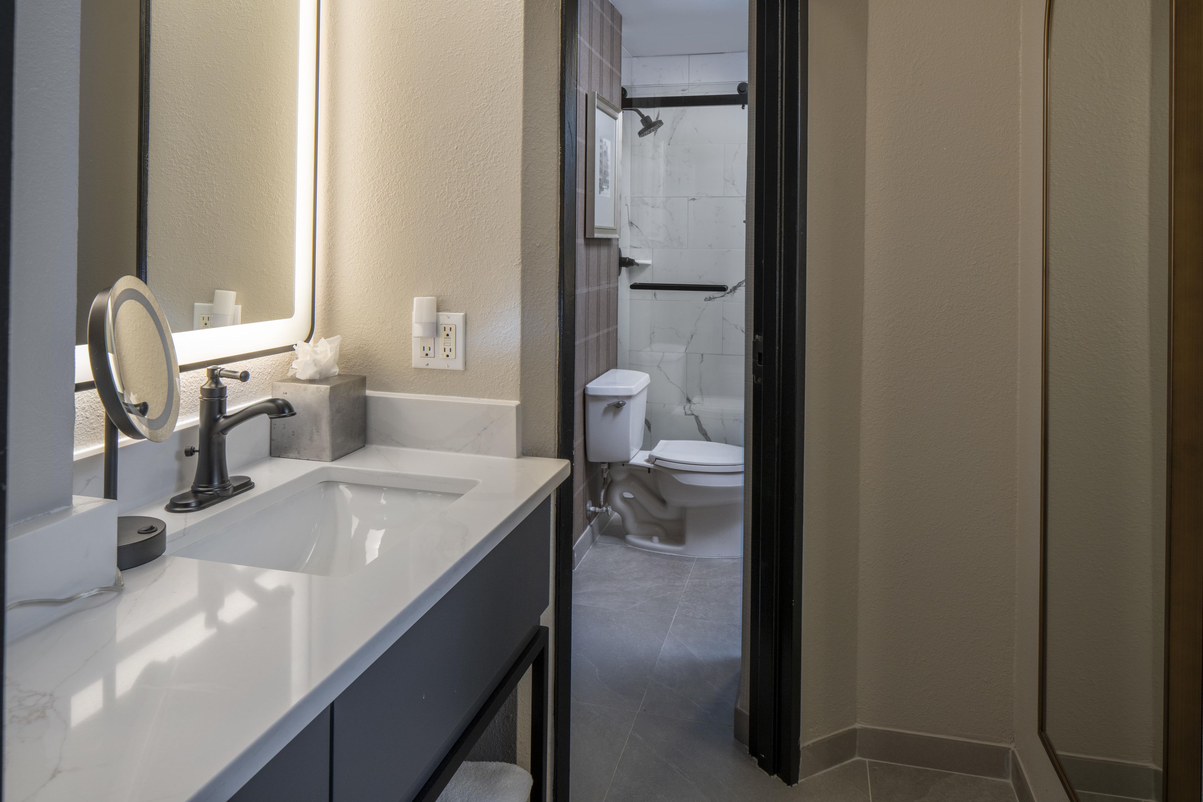A modern bathroom with a white sink, a mirror, and a shower area.