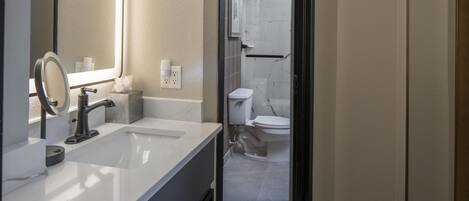 A modern bathroom with a white sink, a mirror, and a shower area.