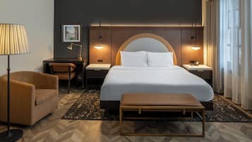 A hotel room with a bed, bedside tables, a lamp, a chair, and a bench.