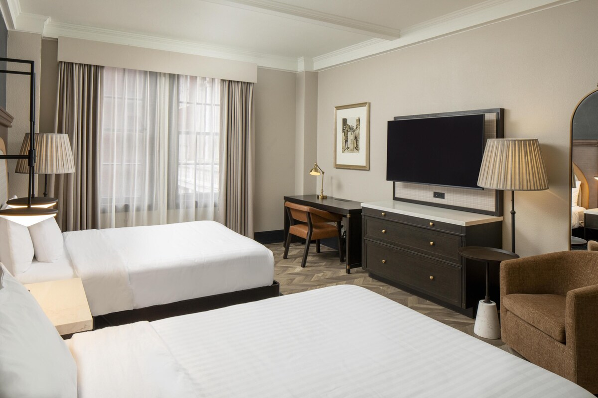A hotel room with two beds, a desk, a television, and a chair.