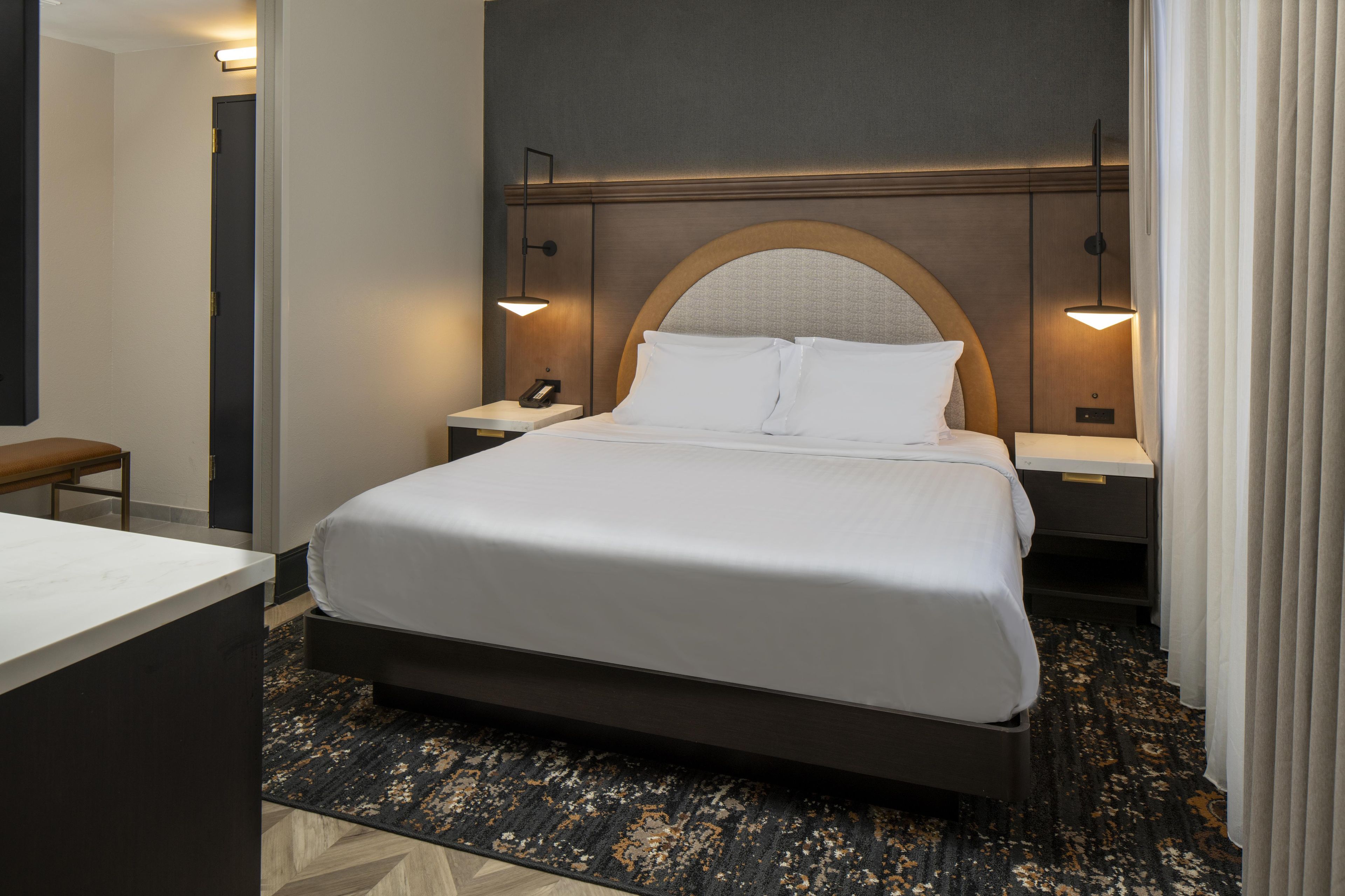 A hotel room with a large bed, bedside tables, a desk, and a chair.