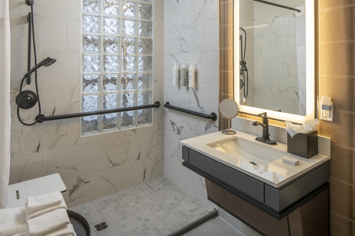 A bathroom with a shower, a sink, a mirror, and a window.