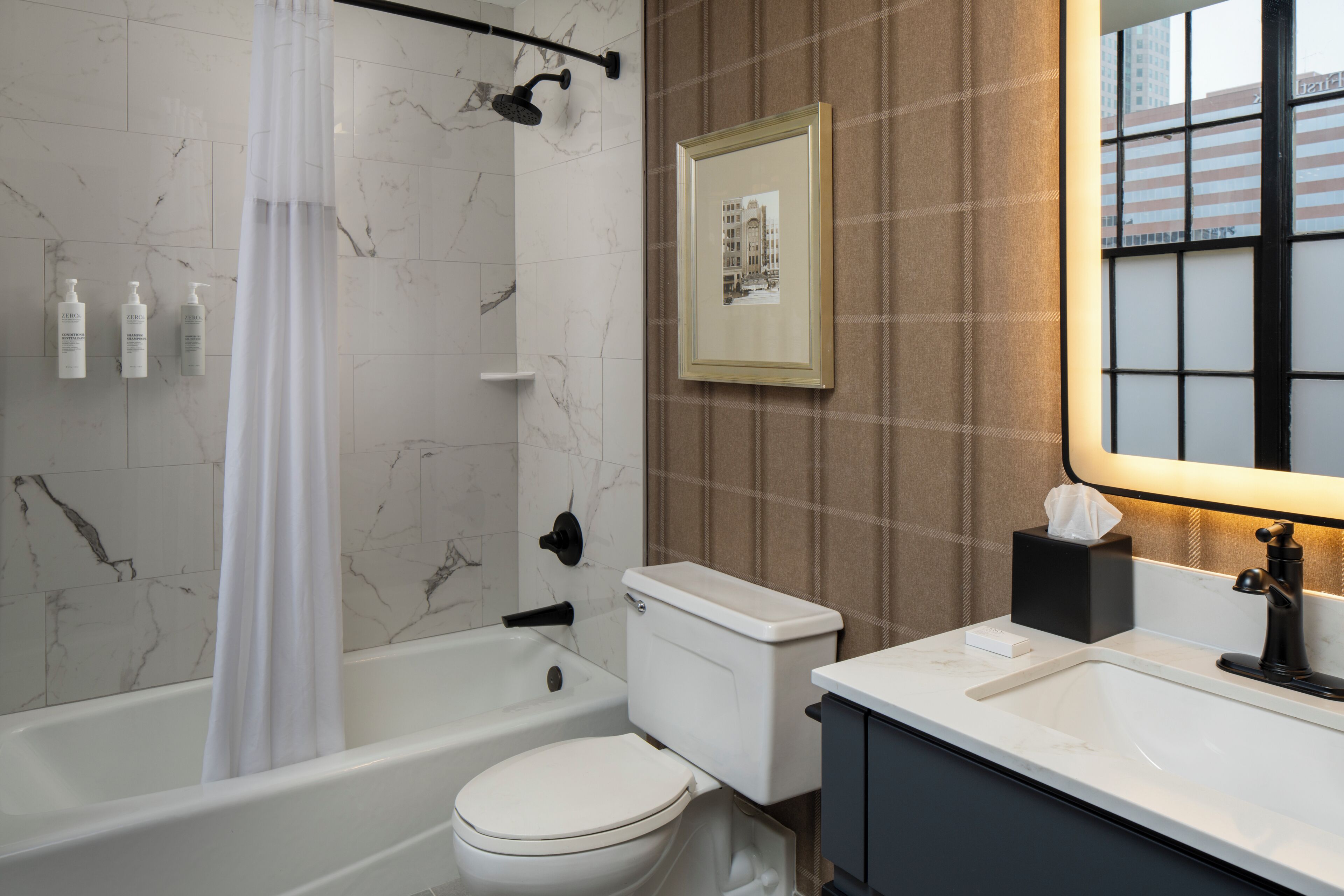 A bathroom with a bathtub, toilet, and sink, marble walls, and a framed picture on the wall.