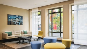 Una hall moderna con divano, poltrone, poggiapiedi e un quadro che raffigura un panorama urbano.