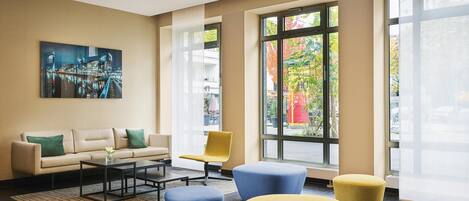 A modern lobby with a sofa, chairs, ottomans, and a cityscape painting.