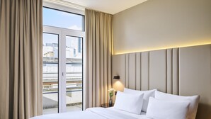 Una camera d'albergo con un grande letto, un comodino con un vaso di fiori e vista sulla città dalla finestra.
