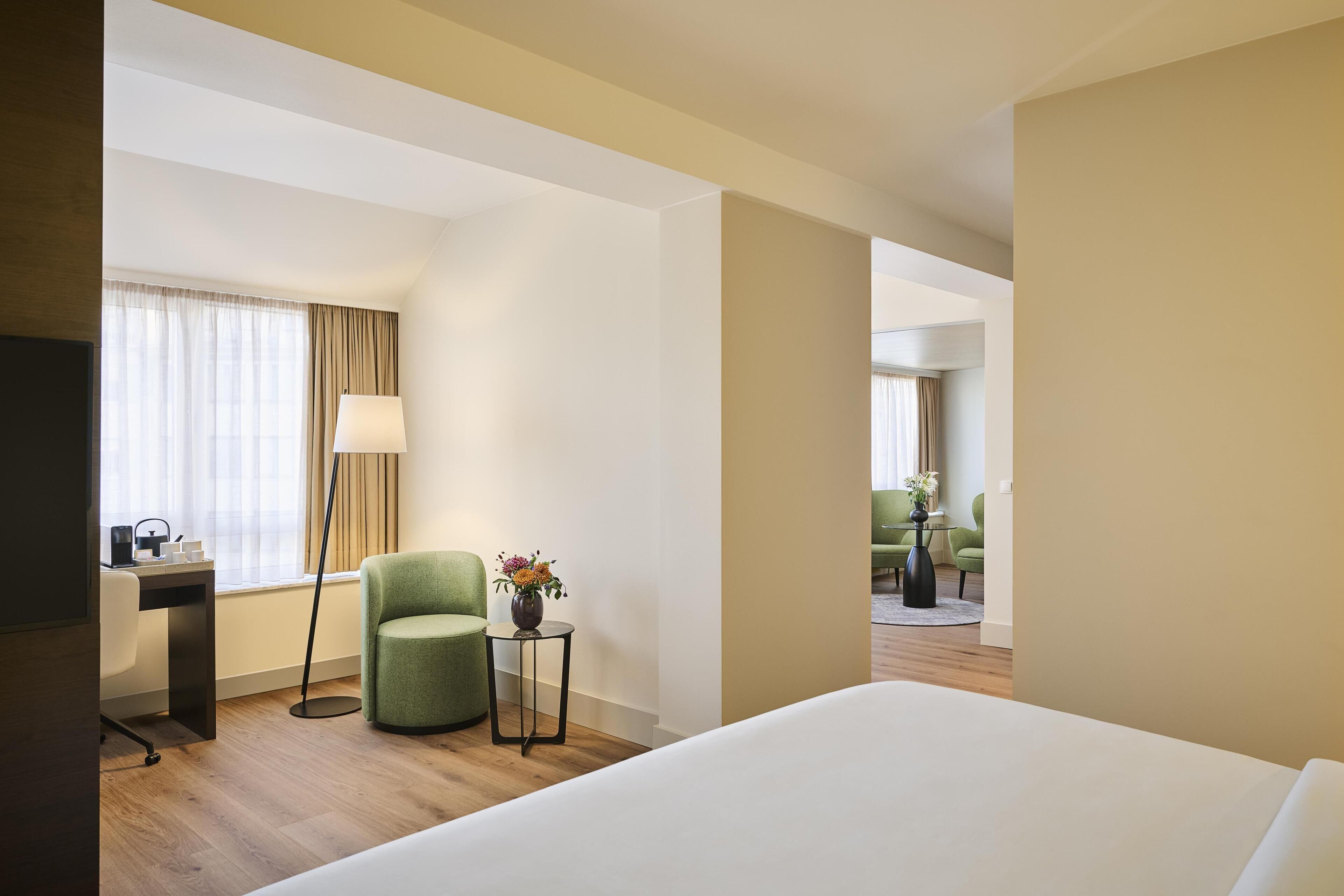 A hotel room with a bed, a desk with a chair, a lamp, and a vase of flowers.
