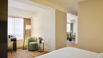 A hotel room with a bed, a desk with a chair, a lamp, and a vase of flowers.