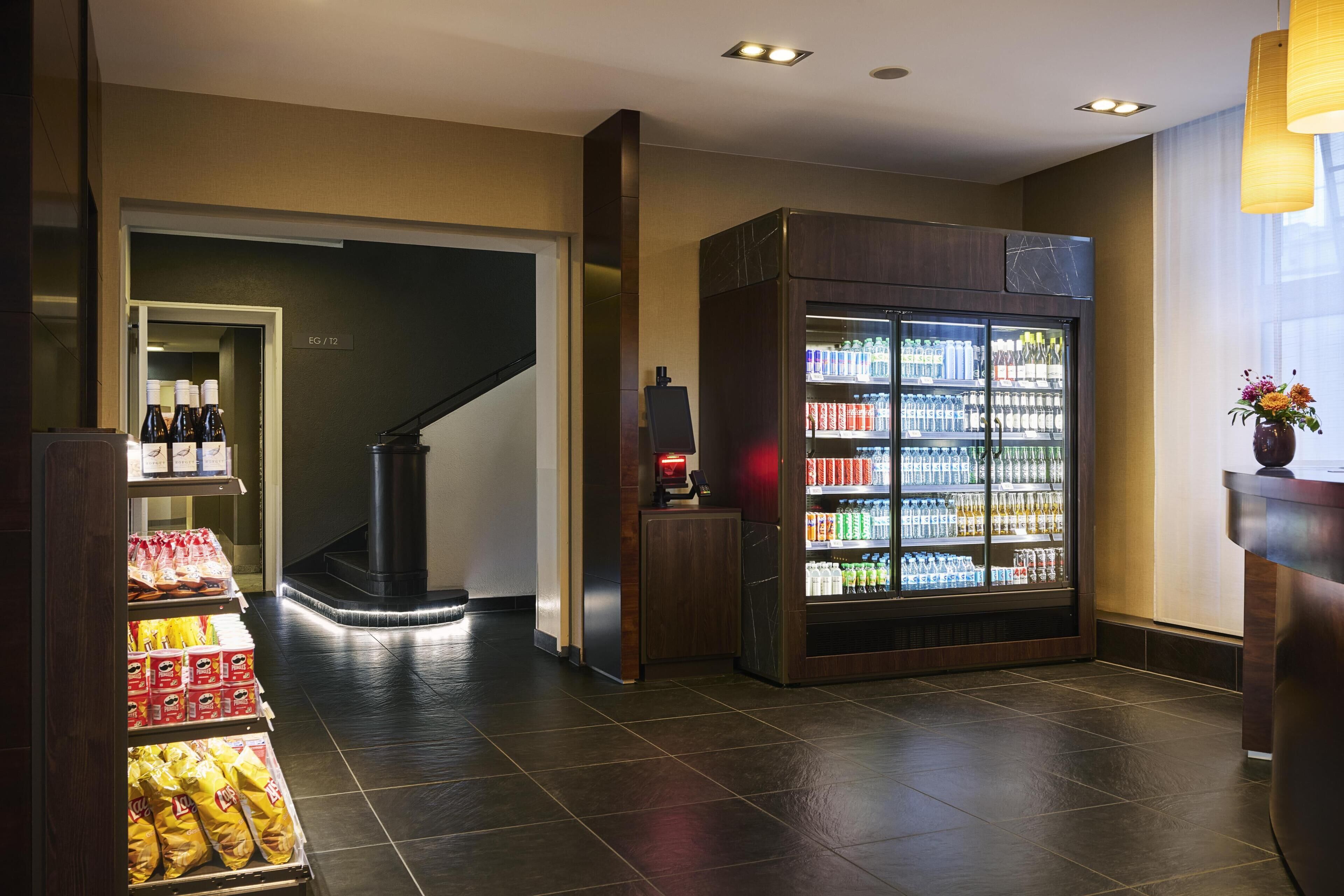 A hotel lobby with a self-service beverage machine, snack vending area, and a staircase leading to another floor.