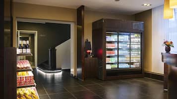 A hotel lobby with a self-service beverage machine, snack vending area, and a staircase leading to another floor.