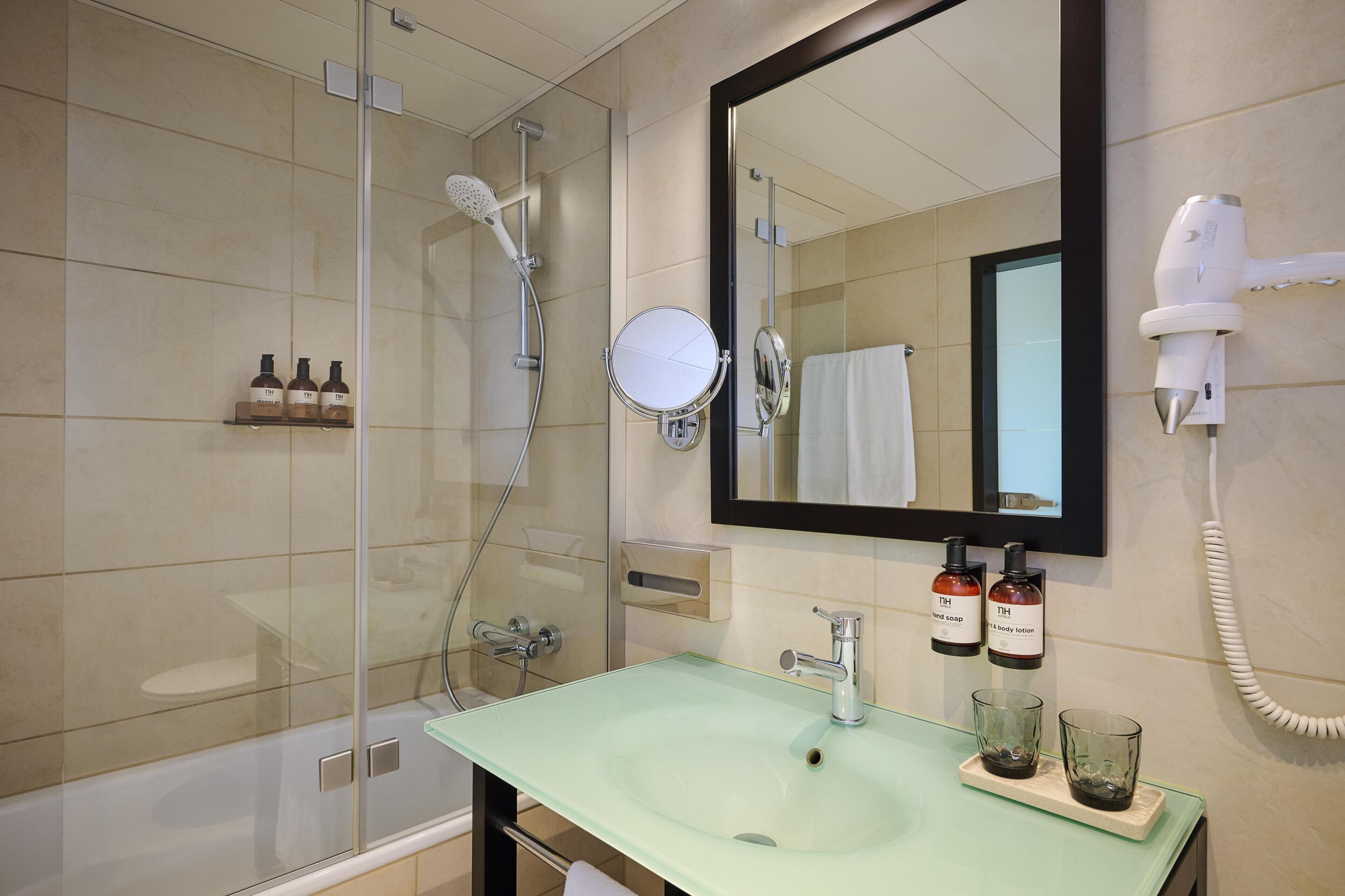 A bathroom with a glass sink, a handheld showerhead, a mirror, and a hairdryer mounted on the wall.