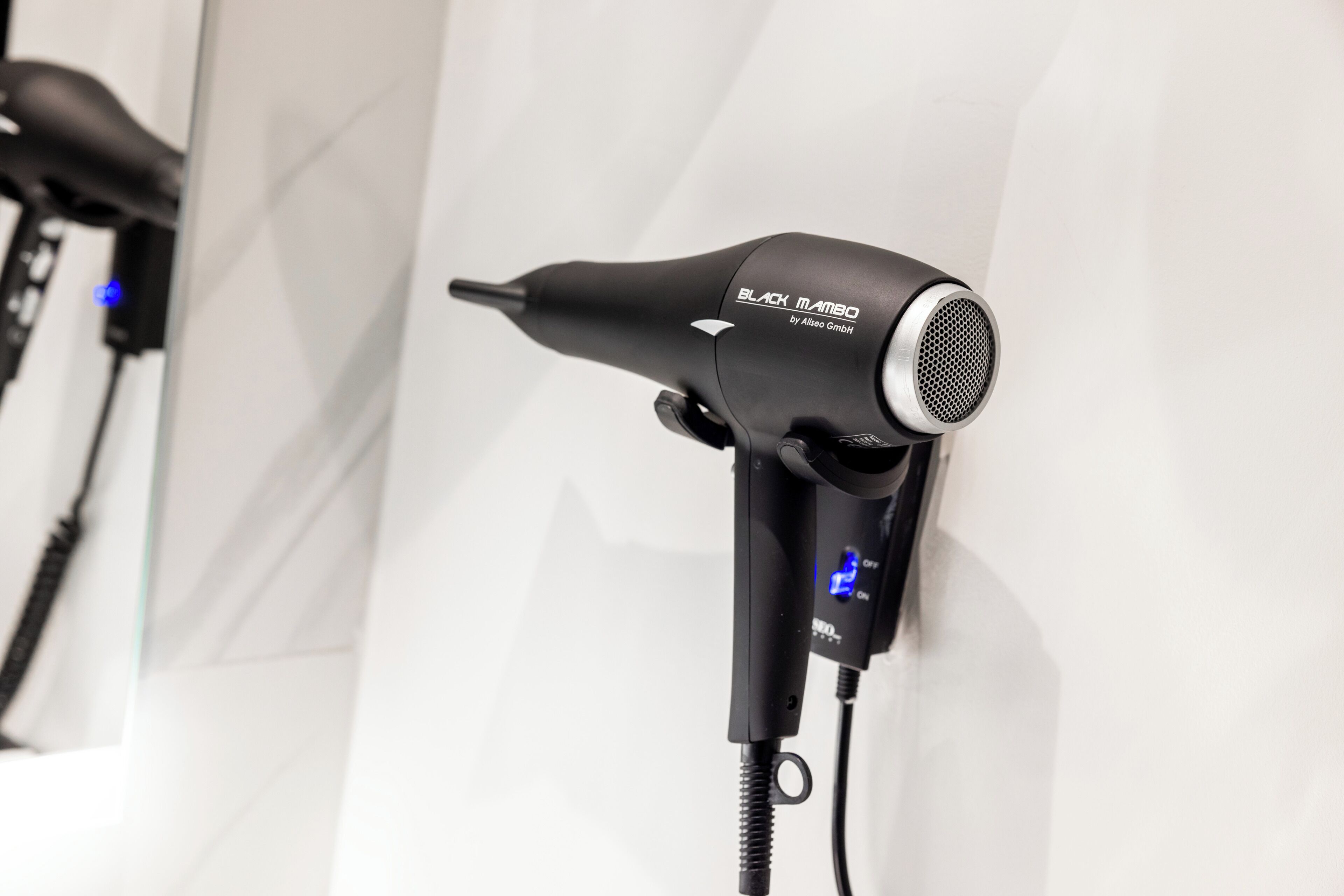 A hair dryer with a digital display and a cord, mounted on a white wall.