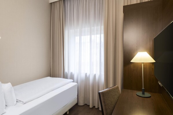 A hotel room with a bed, a chair, a desk, a lamp, and a TV.