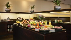 Un buffet con una varietà di cibi, tra cui frutta, verdura e carni, disposti su un bancone con uno sfondo in legno.