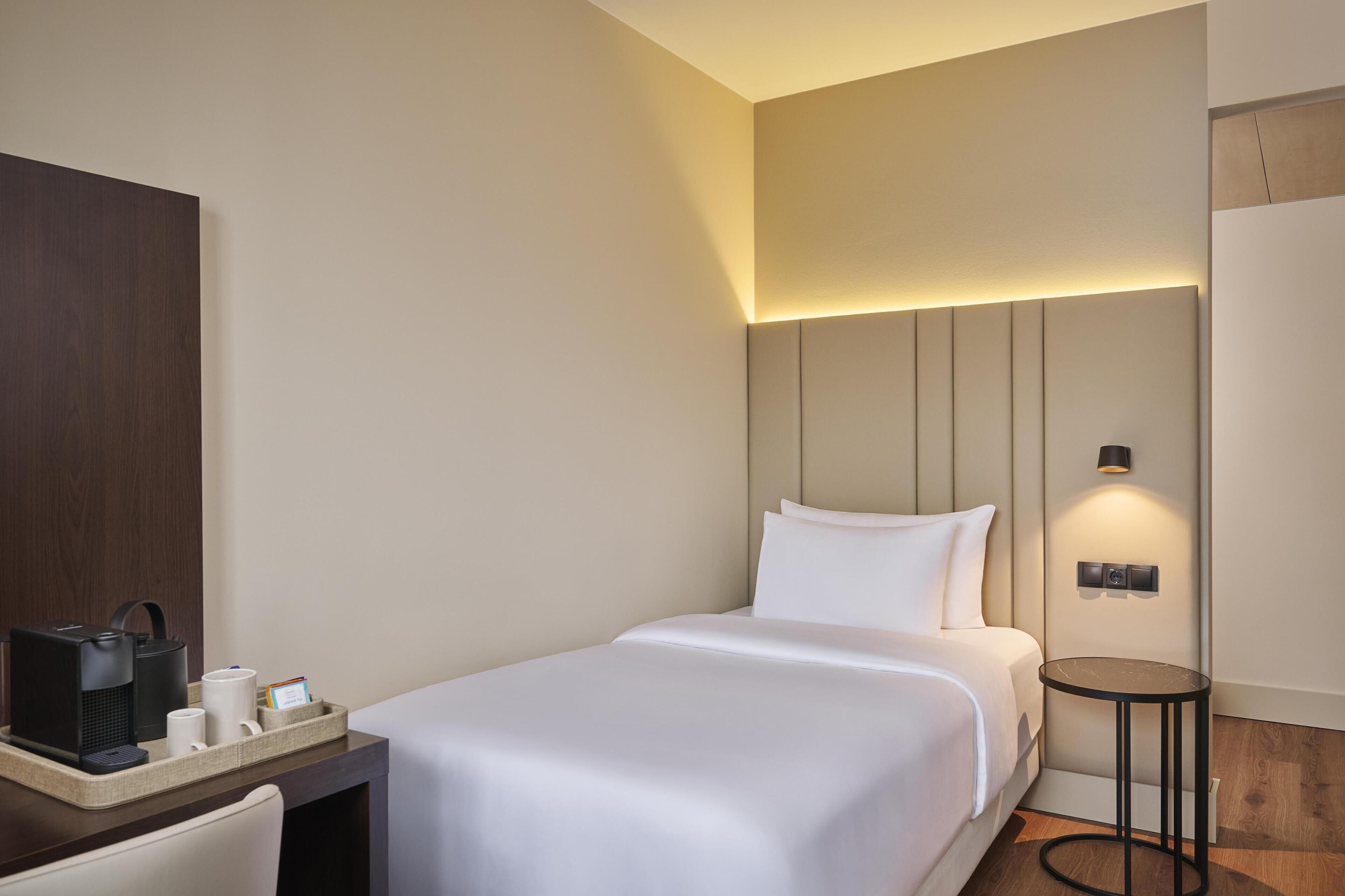 Una habitación de hotel con cama, mesita de noche y una pequeña mesa con lámpara.