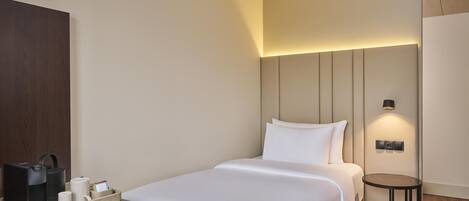 A hotel room with a bed, bedside table, and a small table with a lamp.