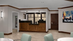 A reception area with a wooden counter, two pendant lights, a refrigerator, and a door leading to another room. - Homewood Suites by Hilton Raleigh/Cary (Cary)