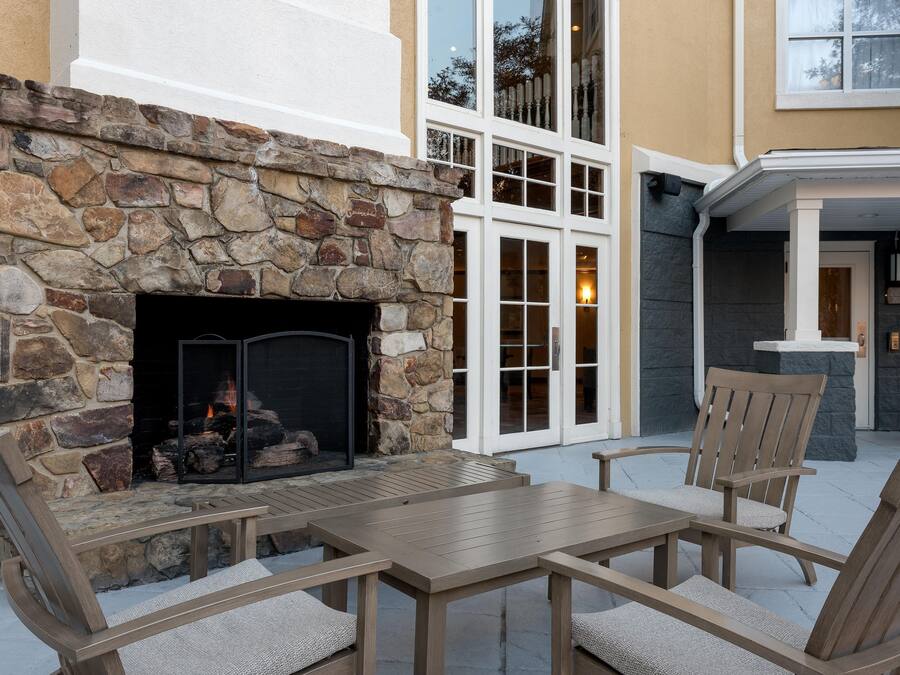 A stone fireplace with a fire, outdoor seating, and a building with large windows and a balcony.