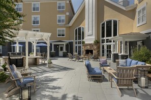 Een overdekt terras met een barbecue, lounge fauteuils en een stenen open haard.
